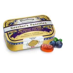 Blaubeer-Vollkonservierte Grether's Pastillen in einer gelben Dose, mit einer roten Pastille und frischen Heidelbeeren daneben.