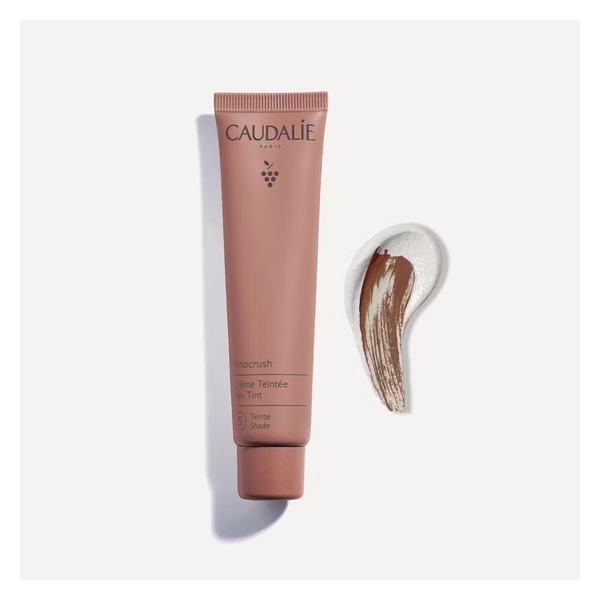 Eine Tube mit getönter Creme von Caudalie neben einem Farbstrich der Creme in einem warmen Braunton.